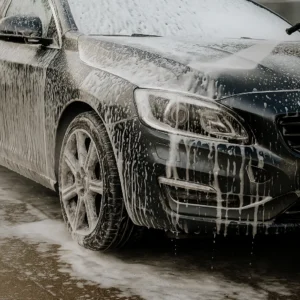 Een auto wordt gewassen met schuim en waterstraal, zichtbaar op de voorzijde en wiel