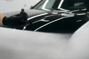 Detailer met zwarte handschoenen brengt zorgvuldig keramische coating aan op een glanzend wit autodak met een microvezelpad in een helder verlichte werkplaats.