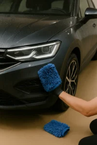 Close up van een donkere metallic auto die wordt gewassen met een blauwe microvezelhandschoen.